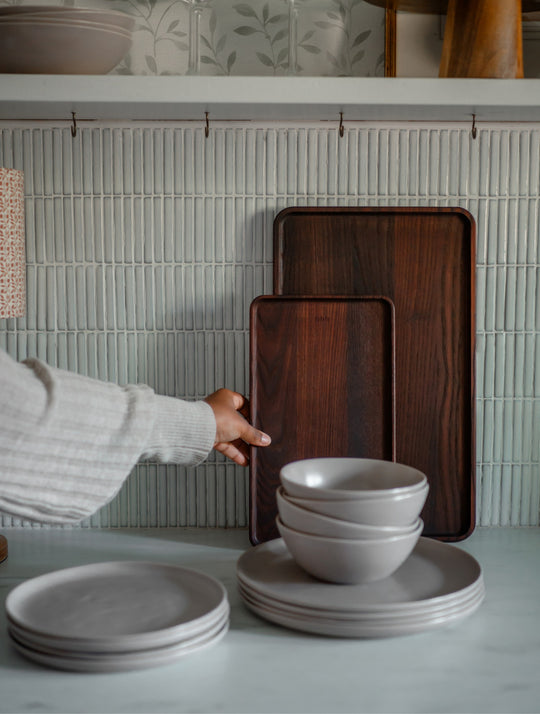Hand reaching for a wooden tray with Fable plates and bowls in the foreground