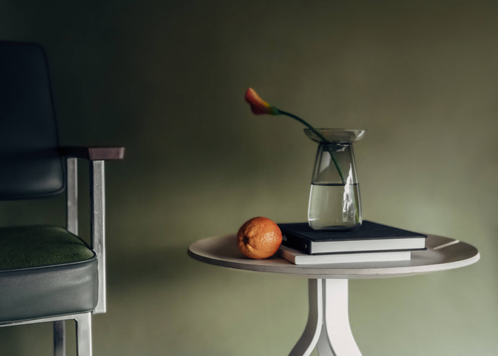 Grey KINTO AQUA CULTURE Vase on a pile of books next to an orange on a white side table, positioned next to a partially visible lounge chair