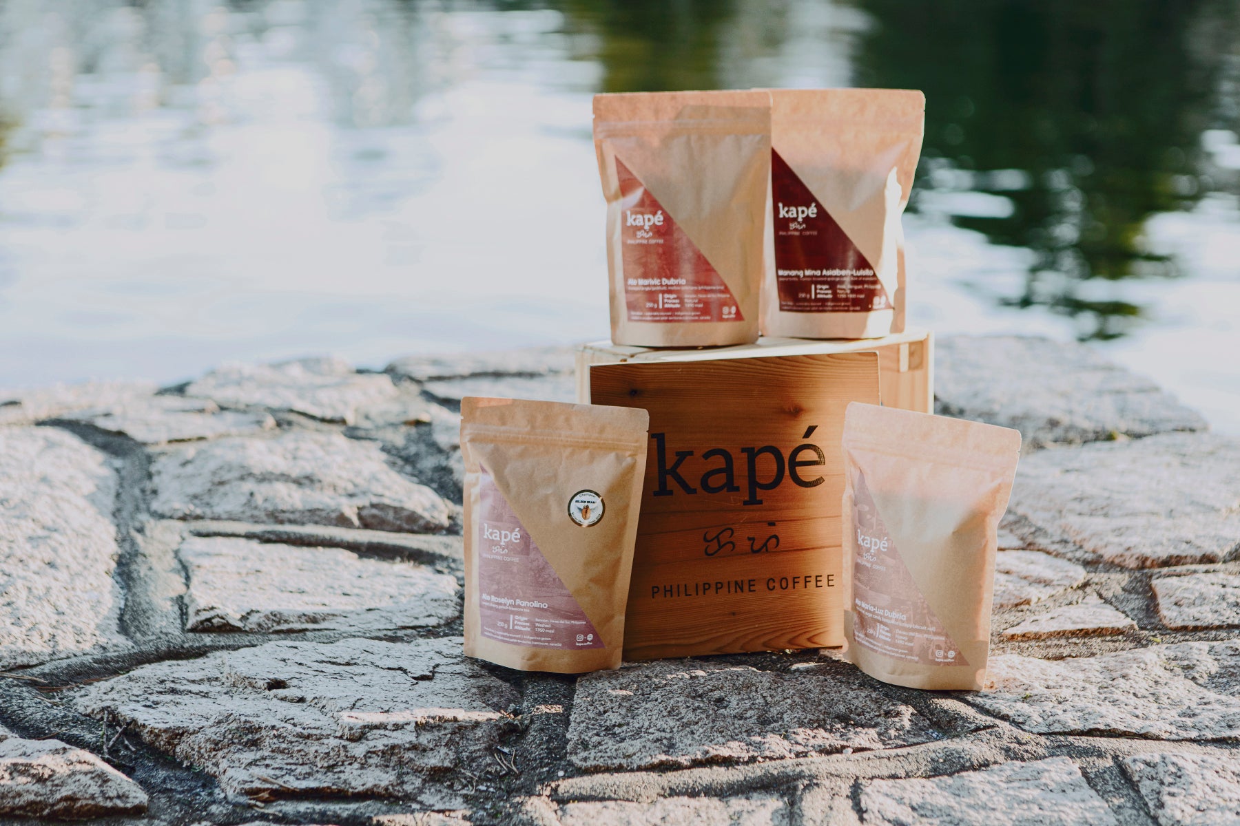 Bags of Kapé Philippine Coffee surround a wooden block by the water. Photo by Issha.