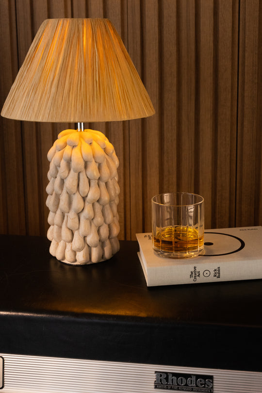 A Rhodes speaker with a goopy ceramic lamp and Fable Rocks Glass on top of a book