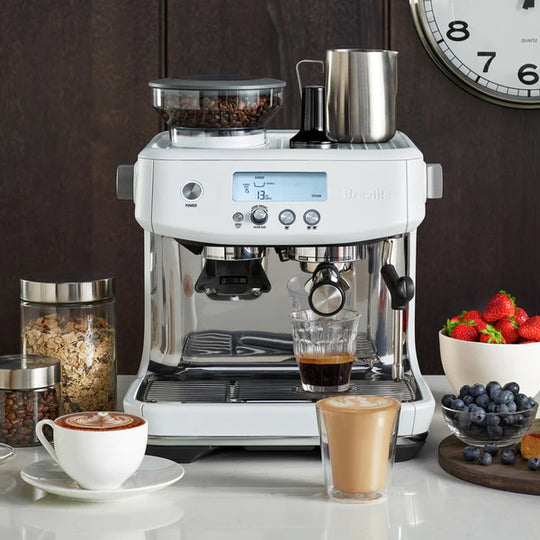 The BREVILLE the Barista Pro™ in Sea Salt on a kitchen counter with cups of coffee, bowls of fruit, and jars of breakfast essentials