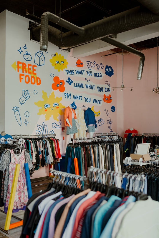 Interior view of Good Neighbour, a pay-what-you-can thrift store, showing clothes on racks and an art wall
